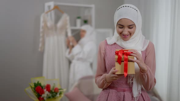 Portrait of Happy Young Excited Muslim Woman in Hijab Looking in Gift Box with Bridesmaid Checking