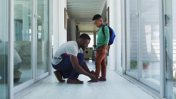 African american father helping his son with tying shoes in hallway