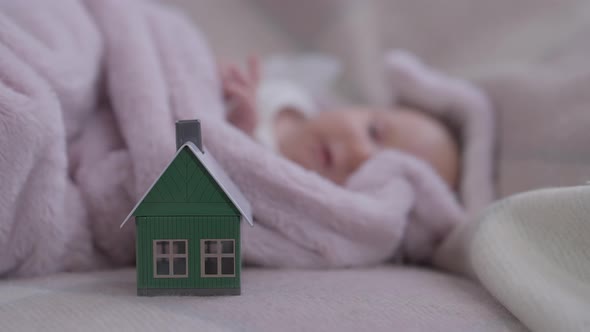 Closeup Toy House on Cozy Bed with Blurred Innocent Baby Girl Sleeping at Background