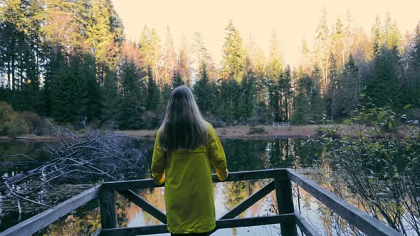 Young Girl in Coat Standing on Terrace Looking at Woodland Landscape in Sunlight