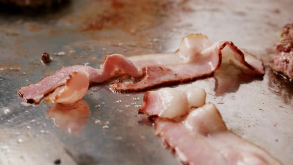 Frying delicious bacon strips in slow motion on a metal plate. Close up