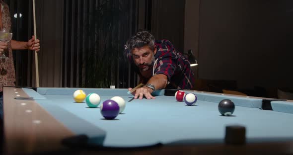 Concentrated player pushing ball with stick cue while playing pool