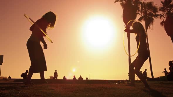 Lens flare shot of two women with hula hoops filmed in slow motion near Venice Beach, California