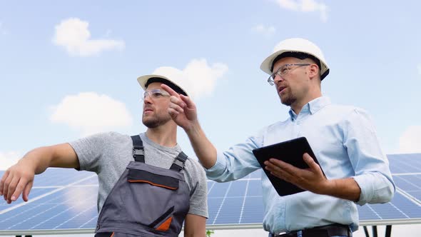 Two Workers in Helmets Check the Installed Solar Panels