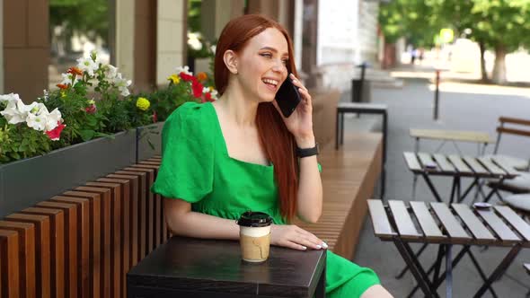 Happy Relaxed Young Woman Talking By Smartphone and Looking Away Sitting at Table with Coffee Cup in