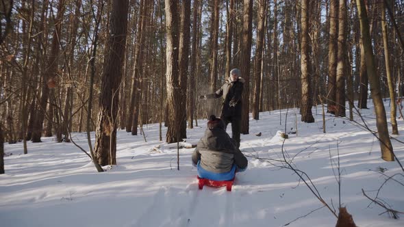 Happy Dad Carries Son on Red Sled in Sunny Snowy Forest