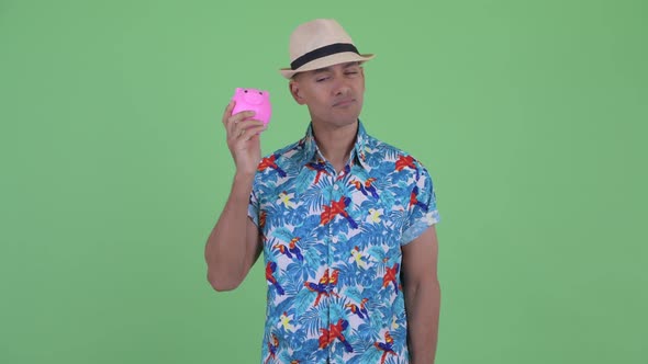 Stressed Multi Ethnic Tourist Man Holding Piggy Bank and Giving Thumbs Down