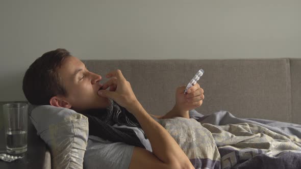 Sick Man Lying in Bed Next To His Medications in His Home and Takes Medicine