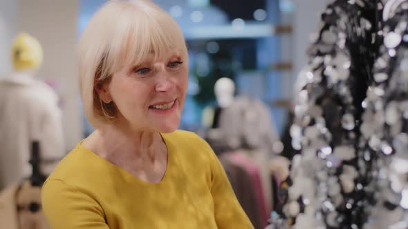 Mature Caucasian Woman Shopper Looks with Surprise and Admiration at Unusual Glitter Dress Female