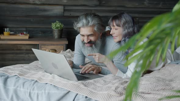 Man and Woman Wearing Pajamas Using Laptop Computer and Chatting Having Fun in Bedroom