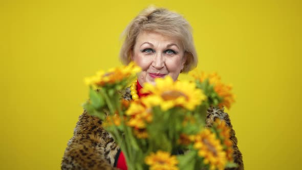 Rack Focus Goes From Smiling Senior Caucasian Woman To Bouquet of Sunflowers Stretched To Camera