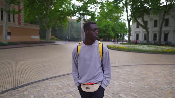 Handsome Young African American Man Walking in City with Yellow Backpack on Shoulders Wearing Casual