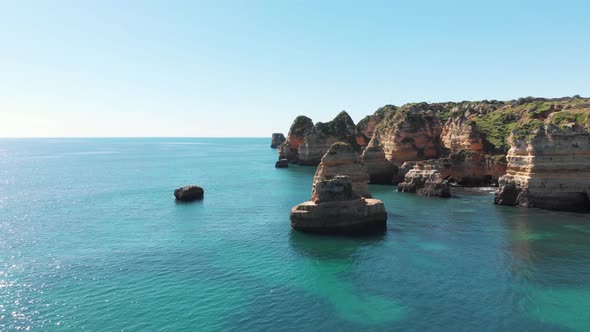 Fly over emerald Atlantic coast of Algarve. Majestic cliffs against blue sky.