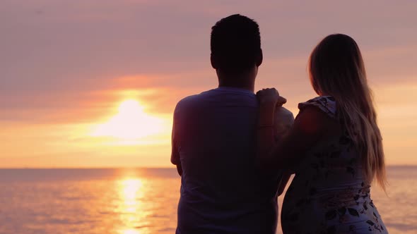 Asian Man with Pregnant Wife Enjoy Sunset Over the Ocean