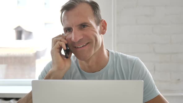 Man Talking on Phone and Using Laptop