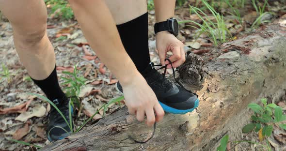 Woman trail runner tying shoelace in forest