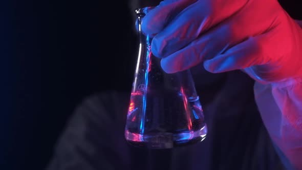 scientist in neon blue red light holds beaker with transparent liquid substance