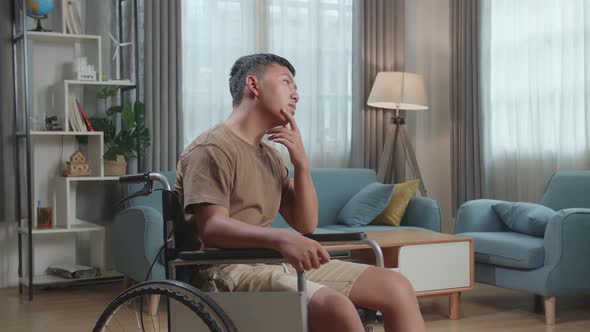 Young Asian Boy Sitting In A Wheelchair And Thinking Then Raising His Index Finger In Living Room