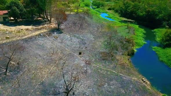 Aerial shot high over a dead field next to a small river