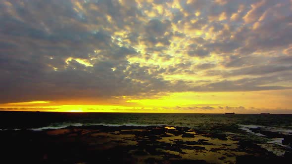 Timelapse footage of a sunrise overlooking a water ladden rock ledge. A sinlge fishermen can be seen