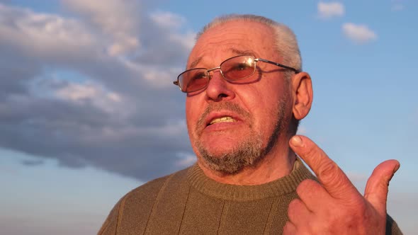 A Grayhaired Man in Sunglasses Speaks Into the Camera Lens Waving His Hand