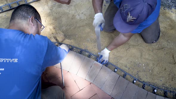 Medium shot of curving brick paving focus on the black edge retainer is held into place by a helper