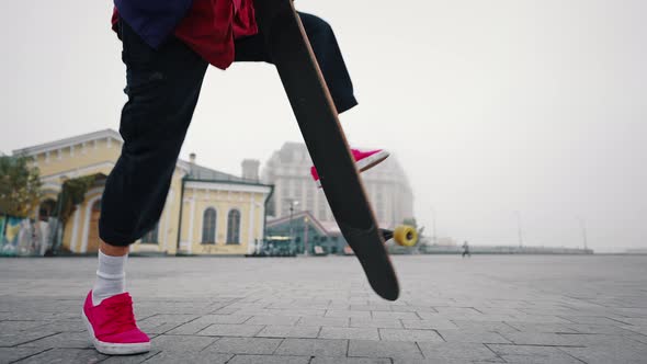 Young Good Looking Skate Boy in a Purple Jacket and Red Shoes is Practicing Longboarding at the