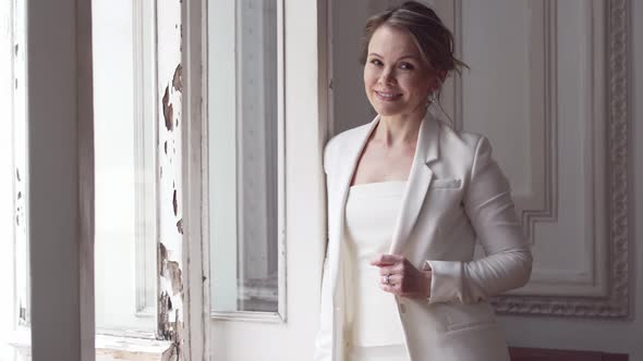 an Attractive Blonde Woman in a White Suit By the Window