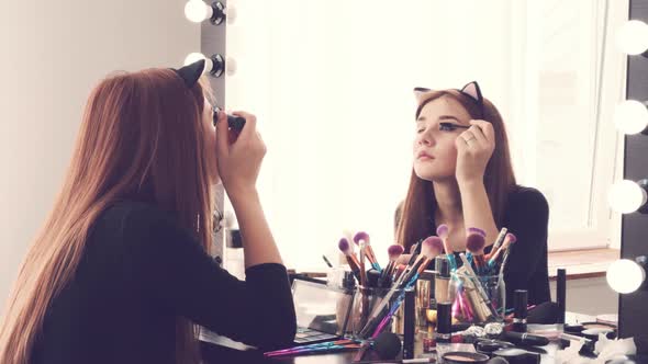 Young Woman Applying Makeup While Sitting at Her Vanity Table with Lots of Cosmetics