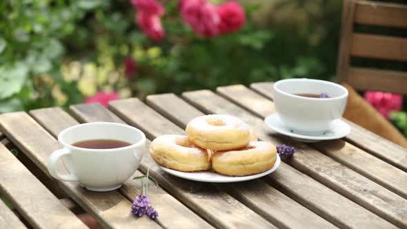 cups of coffee and donuts on a wooden table in a garden with roses on background