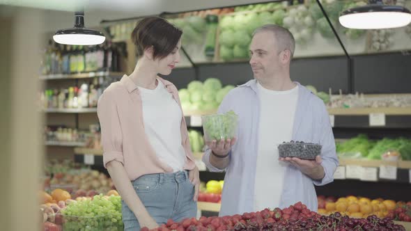 Happy Family Choosing Grapes in Grocery. Portrait of Positive Caucasian Man and Woman Selecting