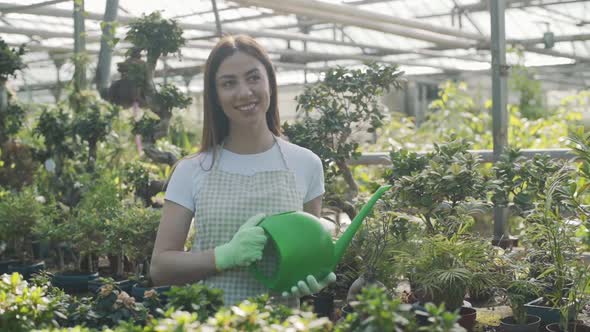 Happy female florist in apron watering houseplants and flowers. The girl takes care of houseplants i