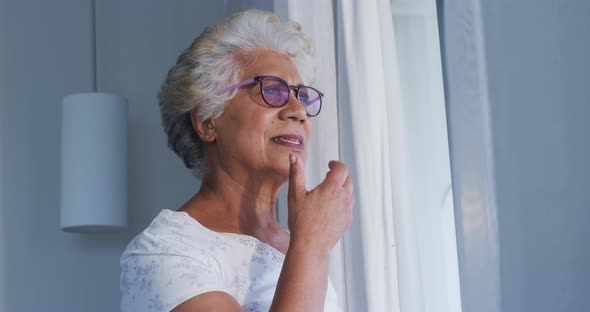 Thoughtful african american senior woman with hand on chin looking out of the window at home
