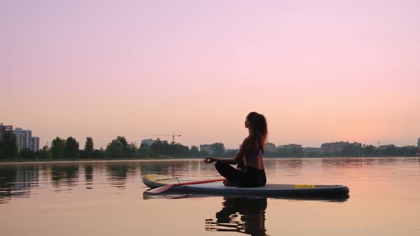 Young Woman Doing Yoga on SUP Board at Sunset