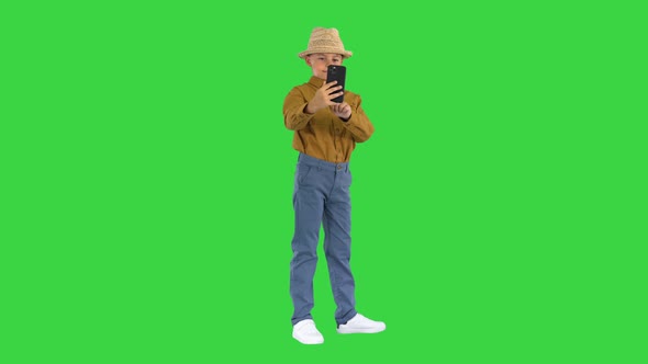 Little Boy in a Straw Hat Taking Selfies on His Phone on a Green Screen Chroma Key
