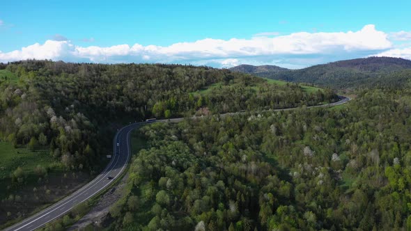 Long Truck Rides Along the Road Climbing Uphill Among Mountains and Forest Aerial View