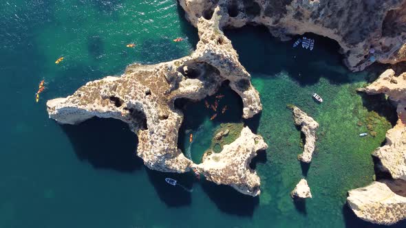 Drone shot of kayaks and boats passing in the ocean, people exploring caves and tunnels.