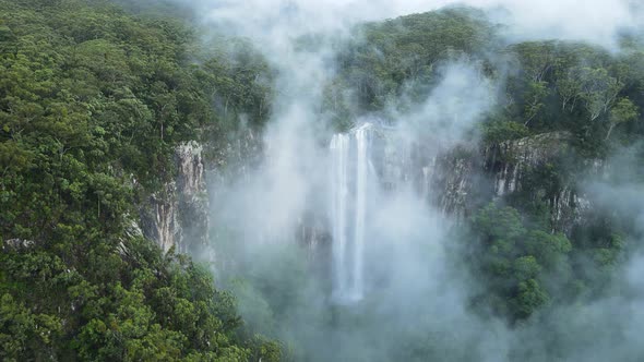 Mist covered mountain reveals a majestic tropical waterfall cascading down a cliff face. Cinematic d