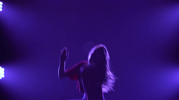 Active Girl Dancer Performs Funky Jazz in a Dark Smoky Studio Against a Background of Blue Lights