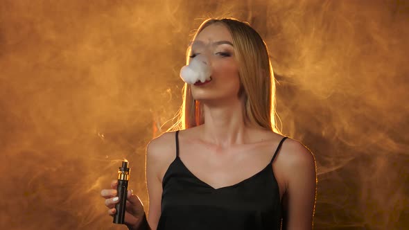 Blonde with Red Lips Smokes an Electronic Cigarette and Smiles. Golden Smoke Background