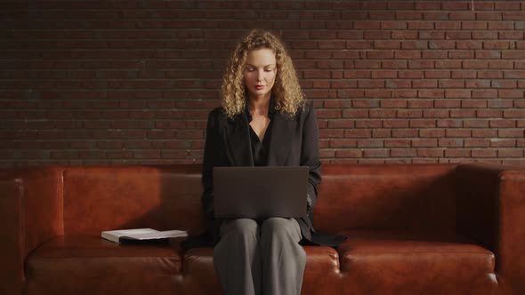 Young Stylish Businesswoman Working on a Laptop in a Loft Apartment with Red Brick Wall