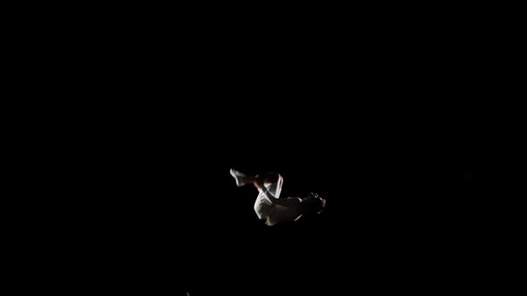 A Handsome Male Gymnast in White Does Acrobatic Stunts on a Black Background in Slow Motion