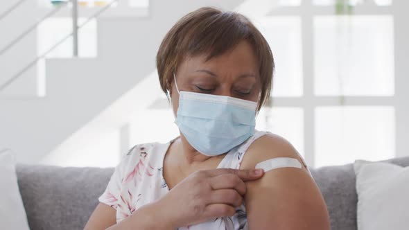 African american senior woman in face mask showing bandage on arm after covid vaccination