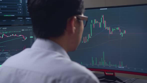 Asian Male Stock Market Broker Looking Analyzing Graphs On Multiple Computer Screens