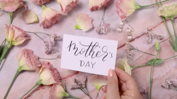 Hand puts MOTHER’s DAY card on a marble table near pink flowers close up