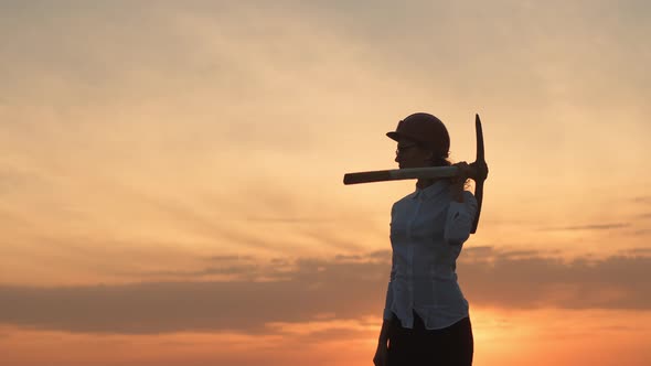 Businesswoman Stands Against Background Sky Outdoor in Helmet with Pickaxe Turns to Face Camera and