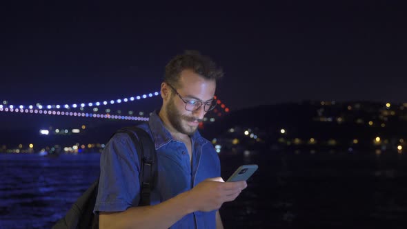 Man looking around smiling and texting. Night.