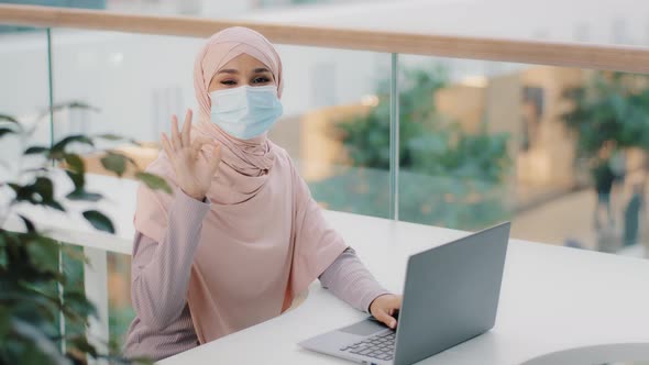 Young Arab Woman Freelancer in Medical Mask Sitting at Workplace Working Typing on Laptop Checking