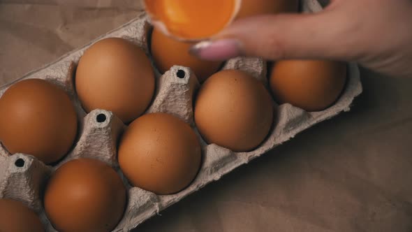 Woman's Hand Puts a Broken Chicken Egg Into a Container with Whole Eggs