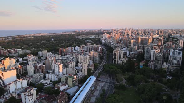 Dolly in flying over a train station surrounded by buildings and parks with Rio de la Plata river in